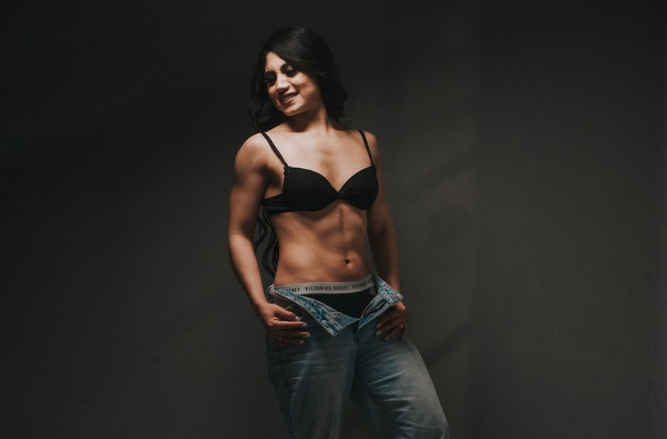 Portrait of a smiling woman in lingerie and jeans showcasing confidence in a studio setting.