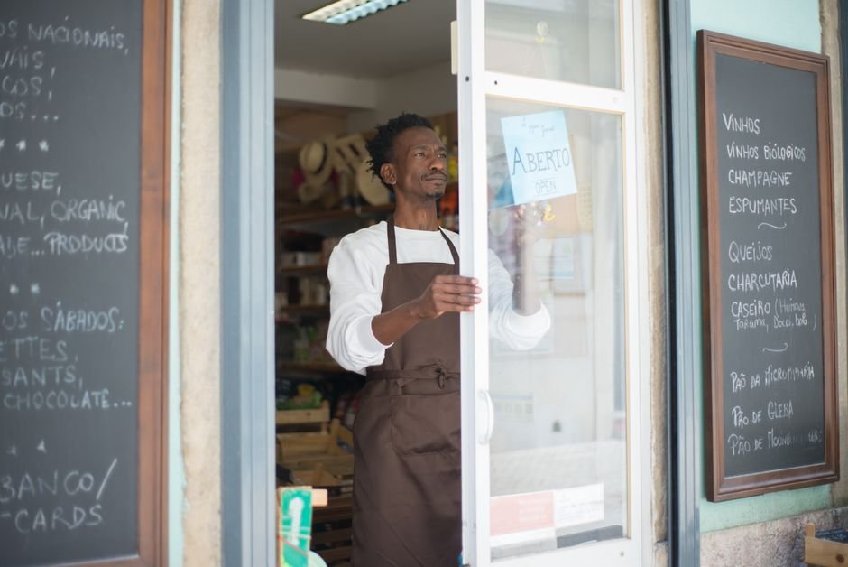 A man in an apron opens a grocery store door in Portugal, ready for business.