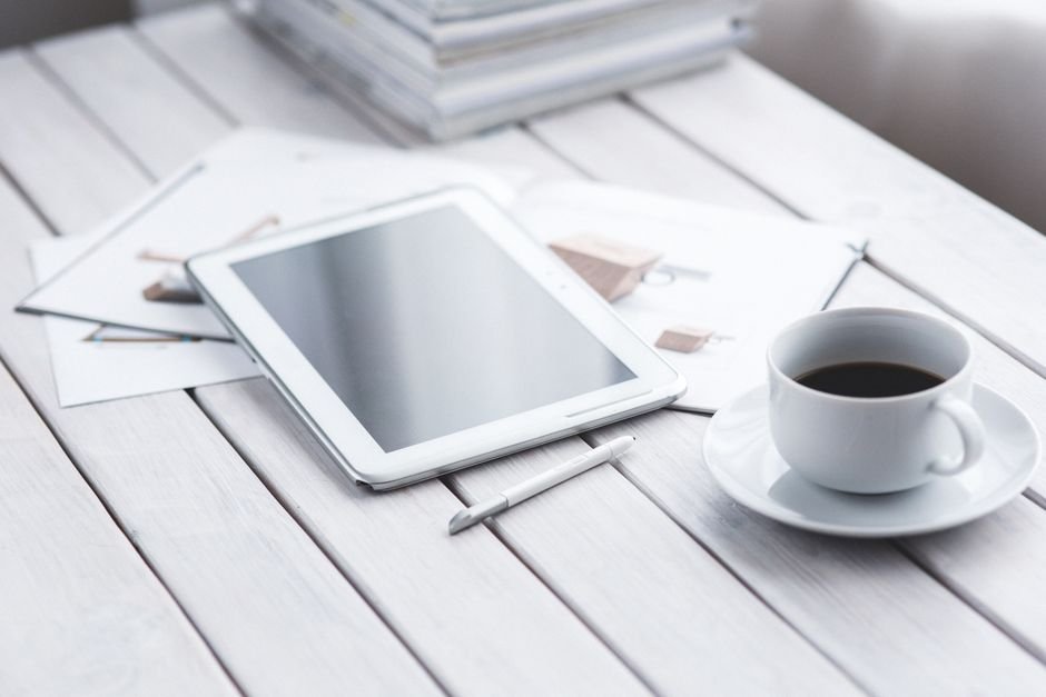 White tablet with stylus and coffee cup on modern office desk setup.