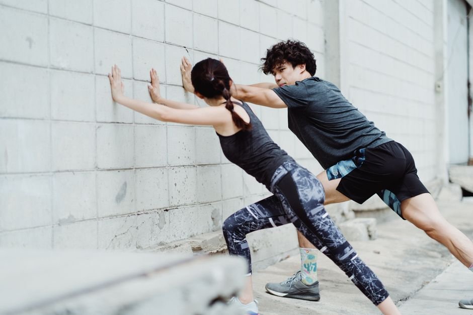 Man and woman stretching against a wall outdoors, showcasing athletic strength and teamwork.
