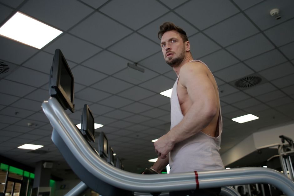 Low angle of muscular adult male athlete in sportswear during training on running machine in modern spacious fitness center while looking away.