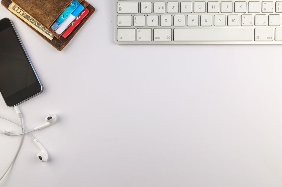 Flat lay of minimalist desk setup featuring a smartphone, keyboard, earphones, and wallet for productivity inspiration.