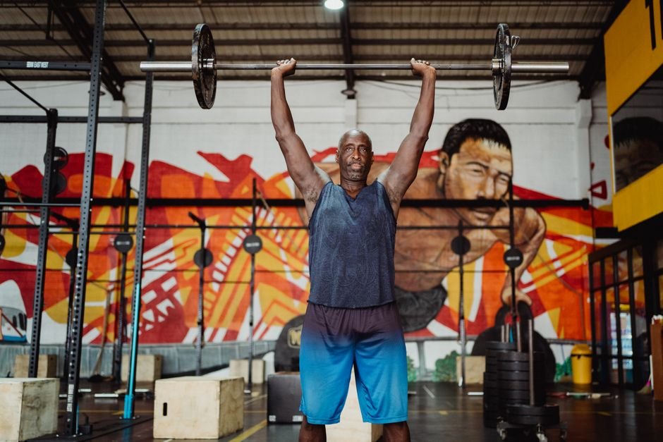 A strong man lifting a barbell in a vibrant gym with murals.