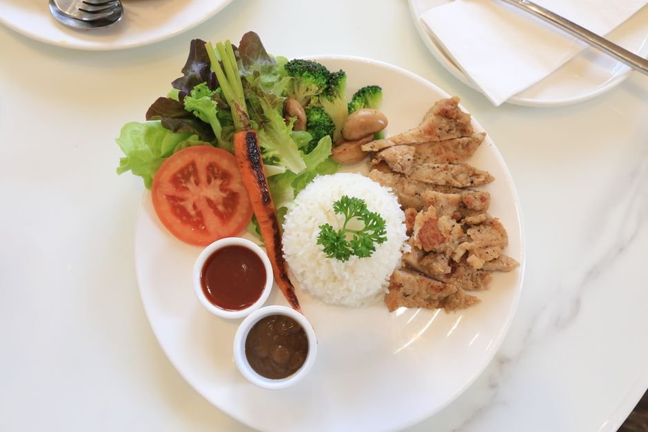 A vibrant plate of grilled chicken, rice, fresh vegetables, and sauces. Perfect for food lovers.