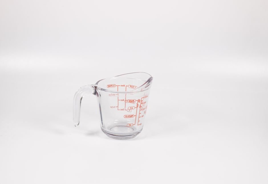 A clear glass measuring cup with red markings on a white background, perfect for culinary use.