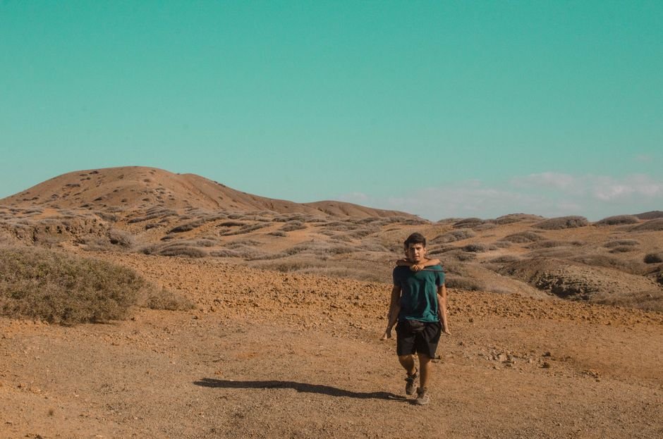 A man walks through a barren desert landscape under a clear blue sky, showcasing solitude and adventure.