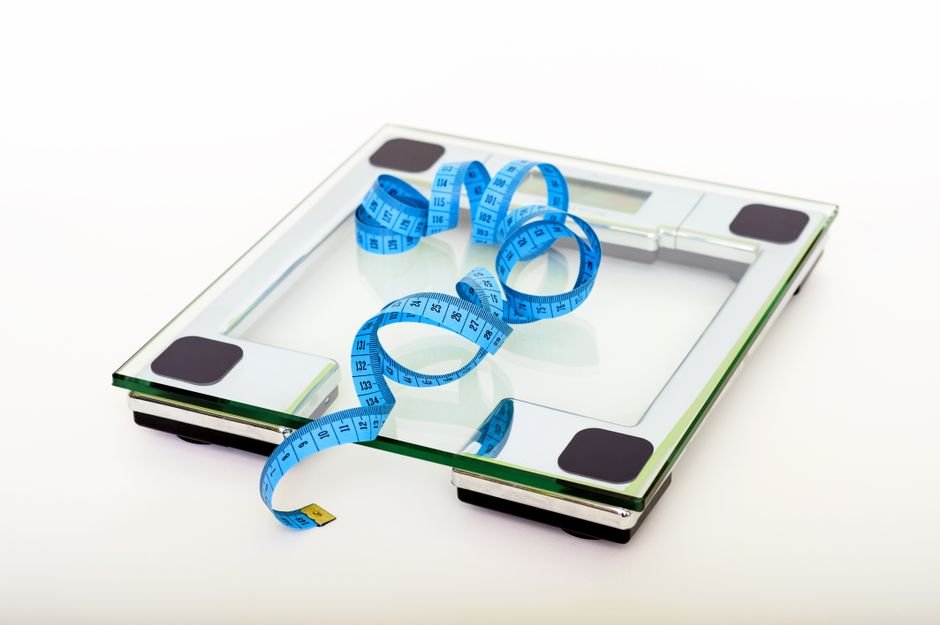 A digital glass weighing scale with a blue measuring tape, symbolizing weight management.