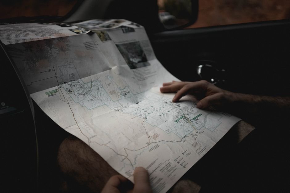 Crop faceless male tourist holding paper map and searching route while sitting in car during trip