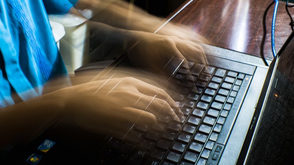 From above of crop anonymous male typing on keyboard in long exposure and sitting at wooden table