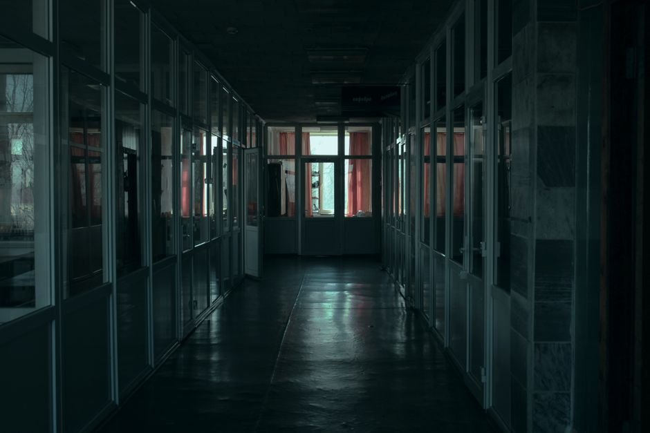 Gloomy indoor corridor with glass partitions and dim lighting in a modern office building.