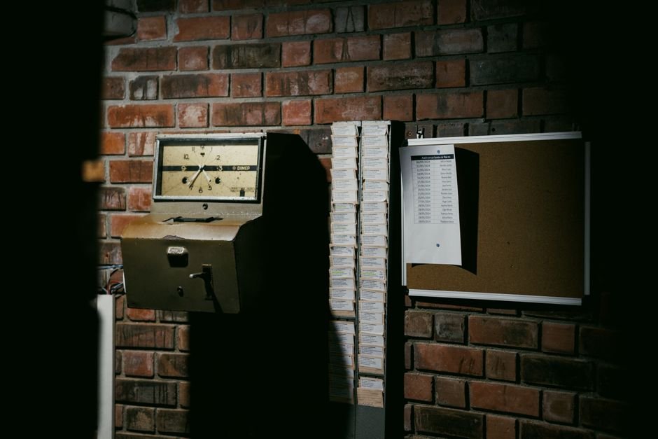 A retro time clock and stack of punch cards against a dark brick wall in an industrial setting.