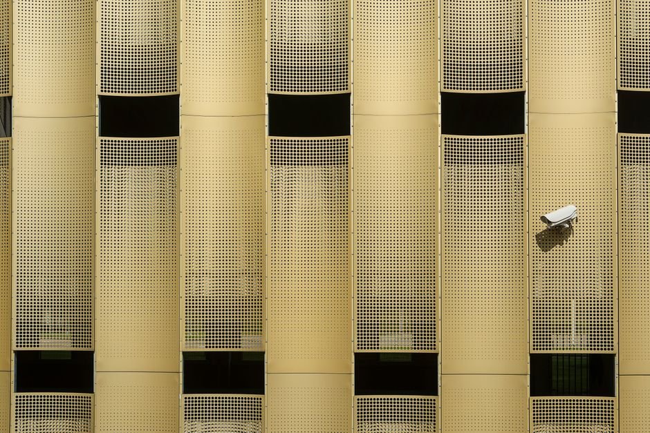 Close-up of a modern building facade with a prominent CCTV camera, showcasing architectural design.