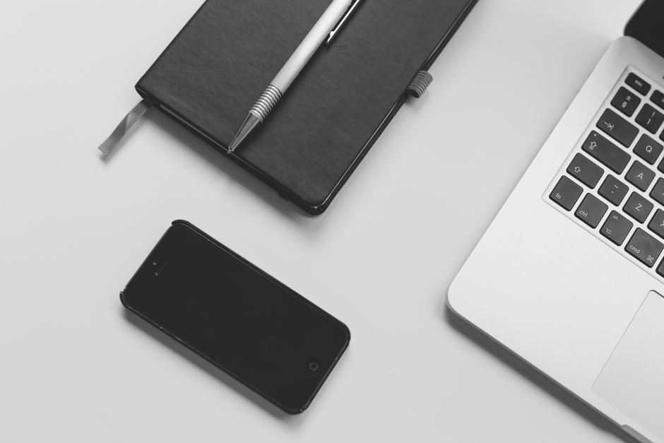 Black notebook with pen, smartphone, and laptop on a clean white desk. Perfect for business and tech themes.