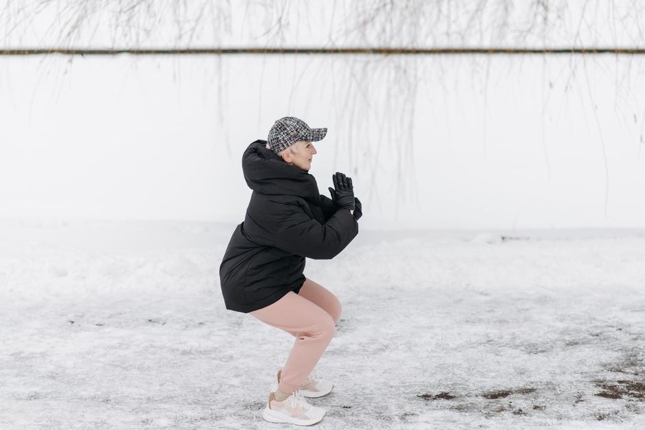 Senior woman in gray hoodie jogging along a park pathway by a canal, embracing an active lifestyle.