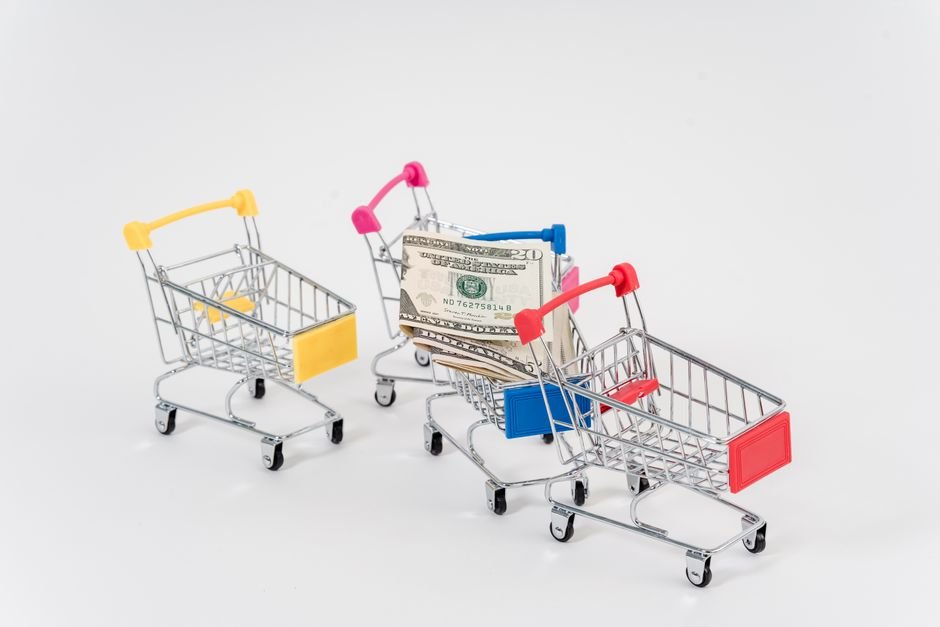 Colorful miniature shopping carts with dollar bills, symbolizing consumerism and finance.