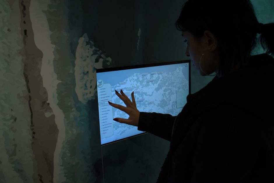 Silhouette of person interacting with a touchscreen map in a dark room.