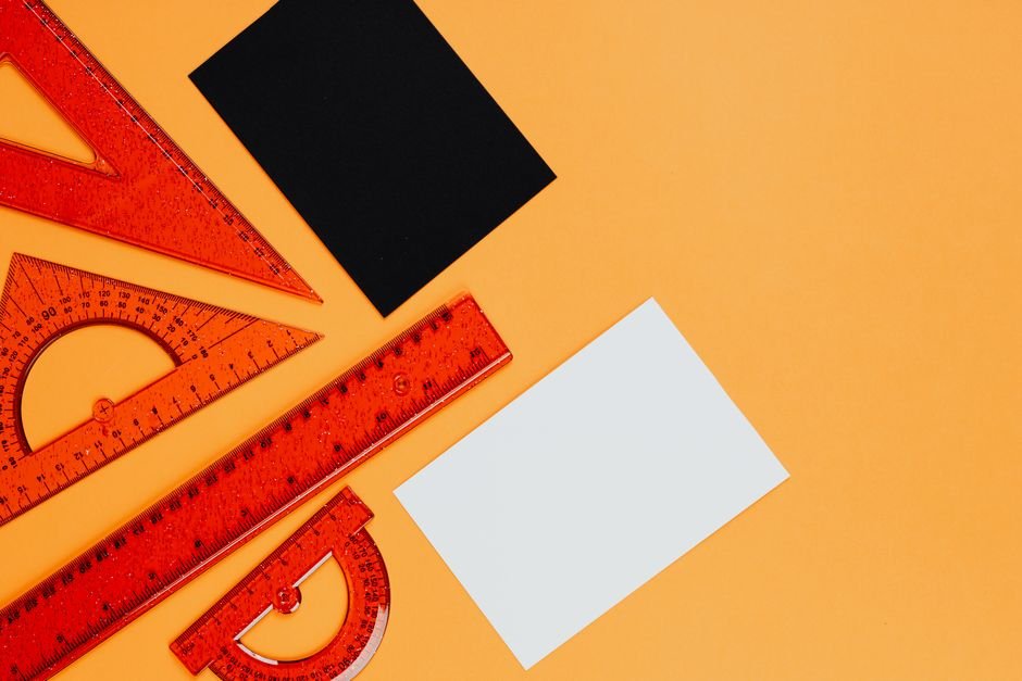 Vibrant orange rulers and geometric tools on an orange background with black and white cards.