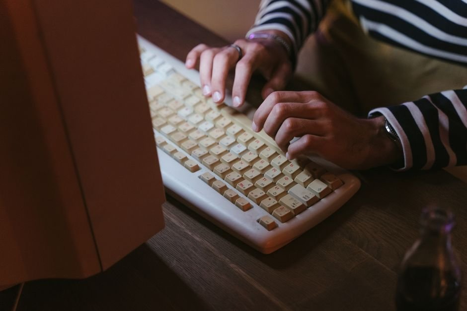 Hands typing on a vintage beige keyboard with a striped sweater visible, indoors.