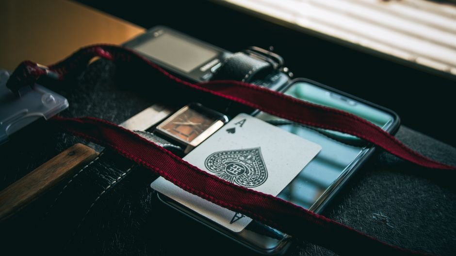 A high-angle shot of a lanyard, playing card, smartphone, and wristwatch on a black surface.