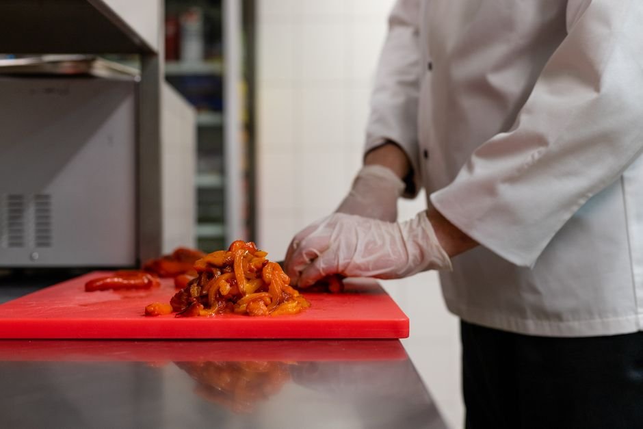 Chef chopping vegetables on a red cutting board in a professional kitchen.