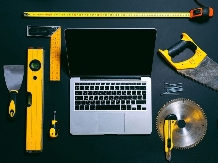 Overhead view of a laptop surrounded by various hand tools on a dark background, representing technology and construction.