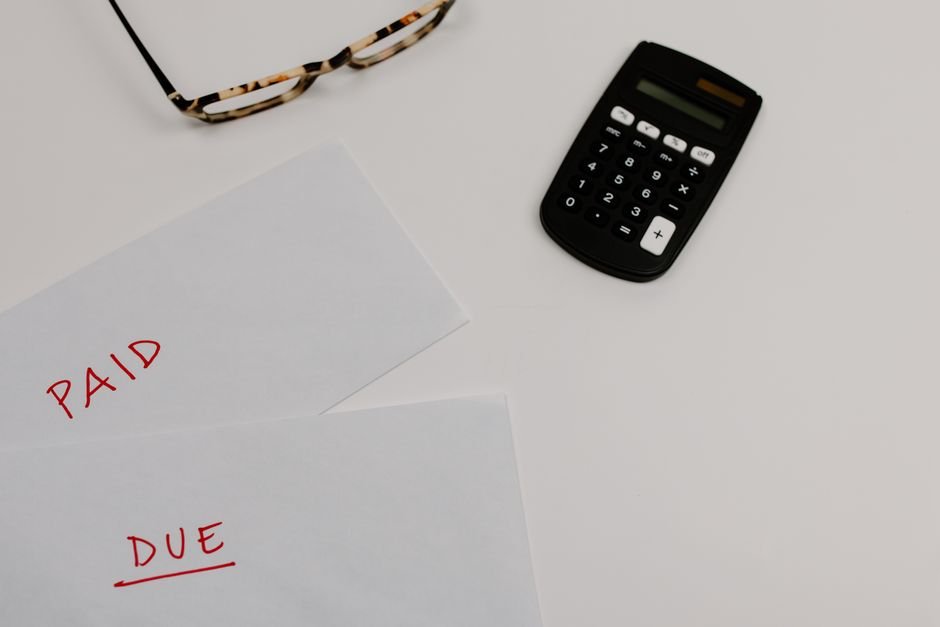 Top view of financial papers labeled 'Paid' and 'Due' beside a calculator and glasses.
