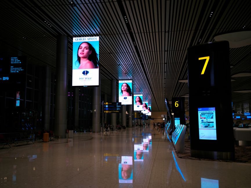Empty airport hallway with digital displays and glossy floors at night.