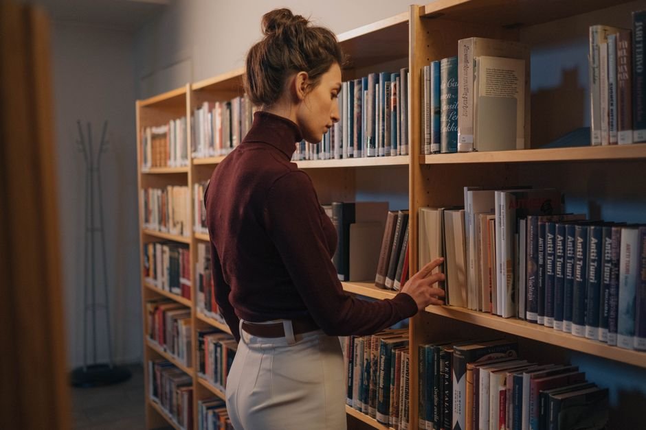 A woman browsing a bookshelf indoors, captured in a peaceful library setting.