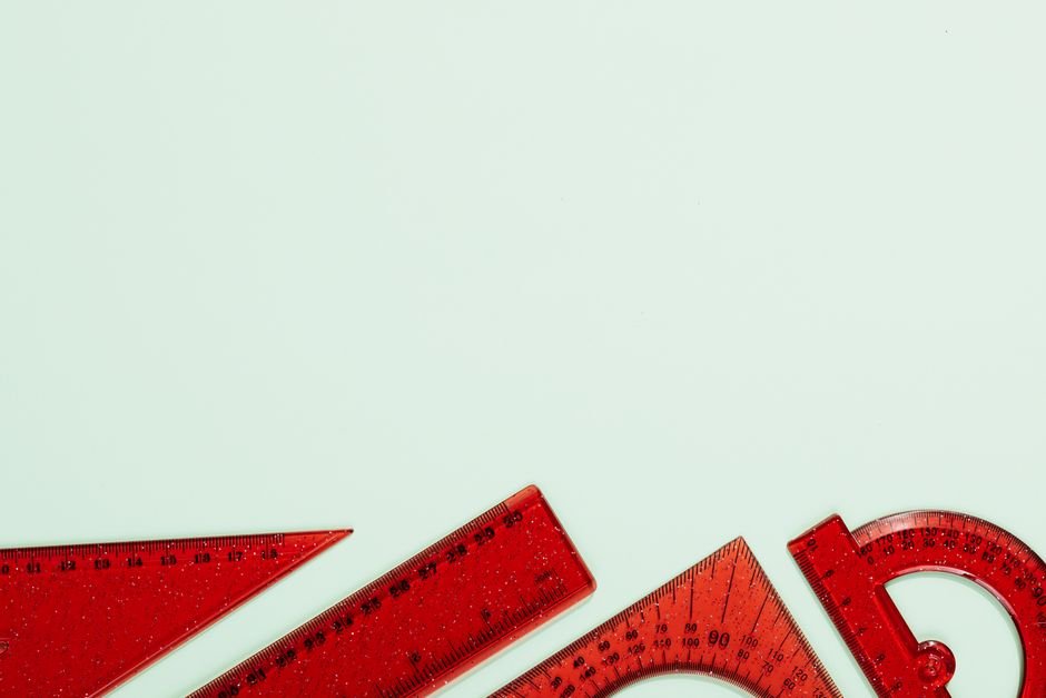 Red plastic rulers and protractors arranged on a soft pastel green background, ideal for school or office themes.
