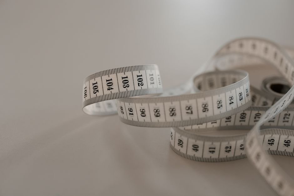 White tape measure with black numbers, coiled loosely on a plain surface.