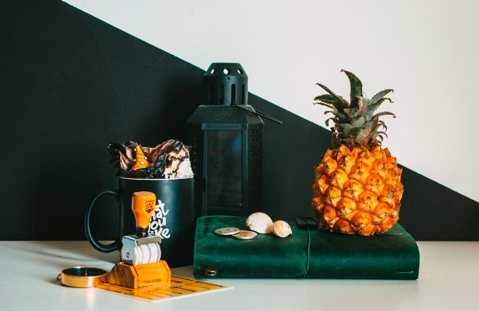 An artistic arrangement featuring a pineapple, lantern, and decorative objects on a black and white background.