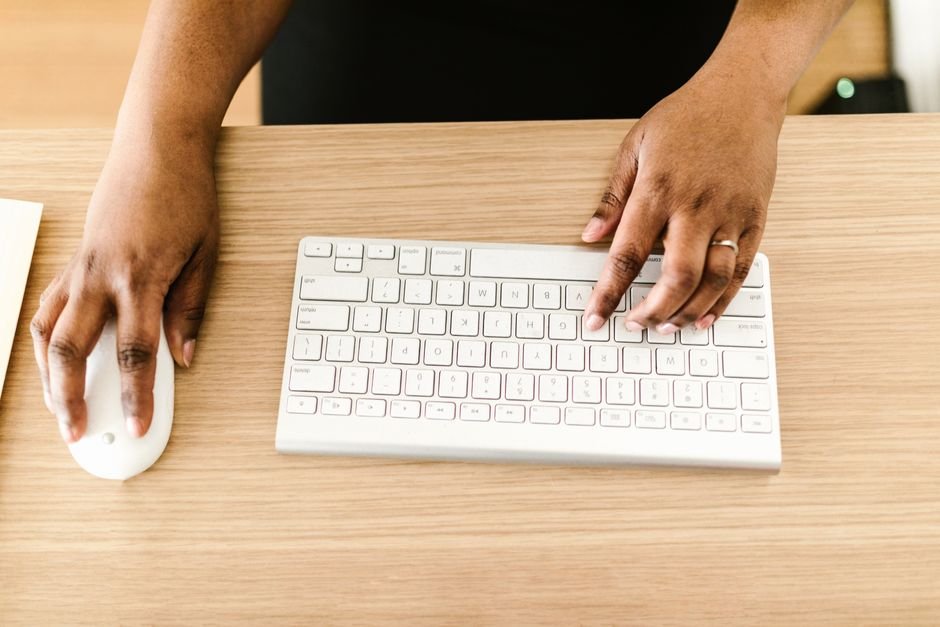 Hands typing on a white keyboard on wooden desk, ideal for business or tech themes.