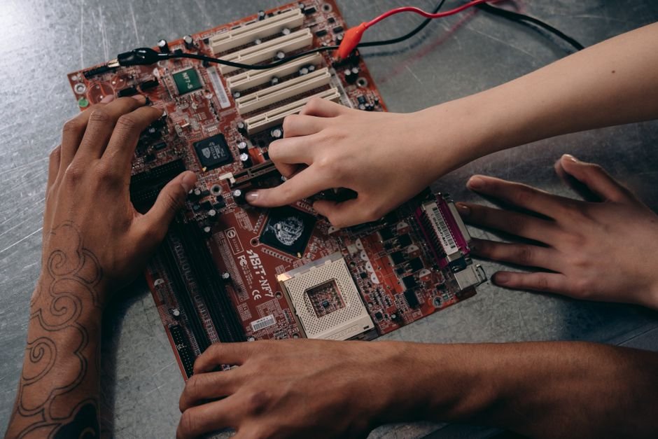 Close-up of hands repairing a motherboard, highlighting teamwork and electronics engineering.
