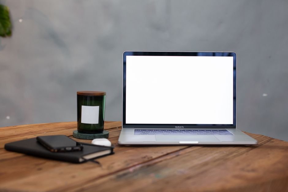 A modern workspace featuring a blank laptop screen, notebook, and candle on a wooden table.