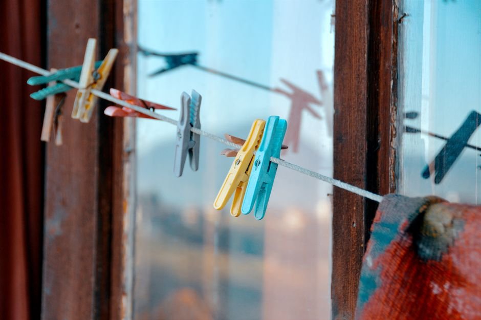Vibrant clothespins hanging on a clothesline by a rustic window.