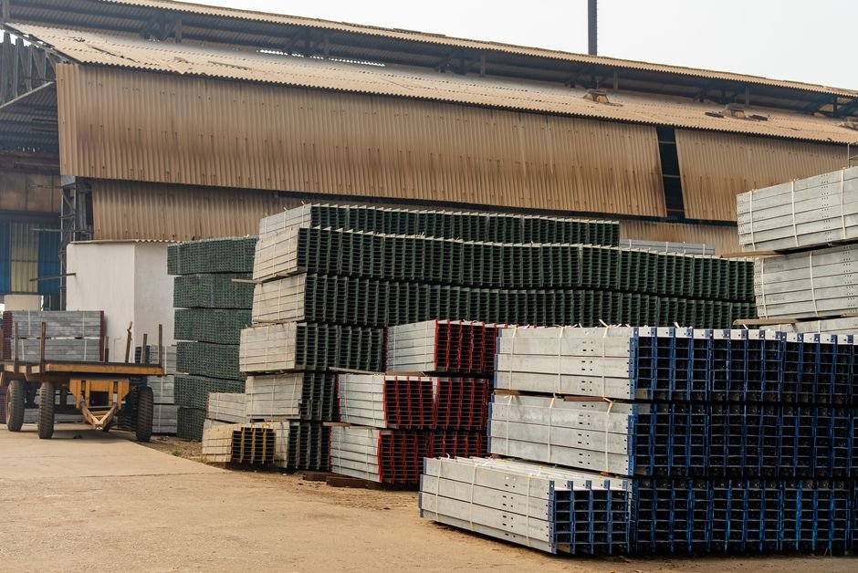 Outdoor view of an industrial warehouse with multiple stacks of metal beams and pallets.