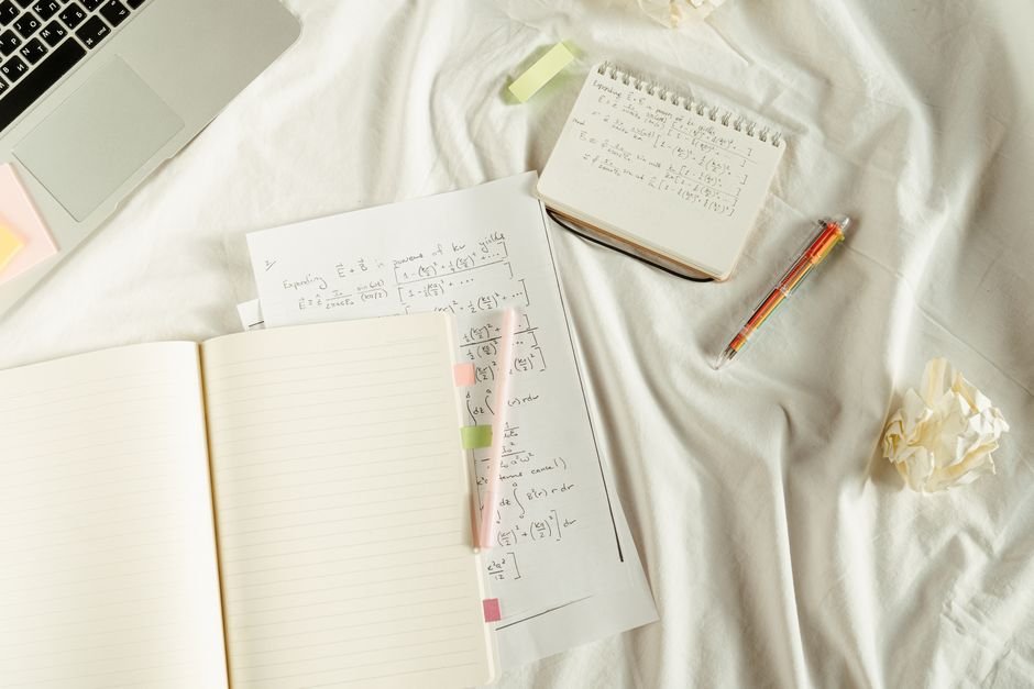 Flat lay of a cozy study space with notebooks, math formulas, and laptop on bed.