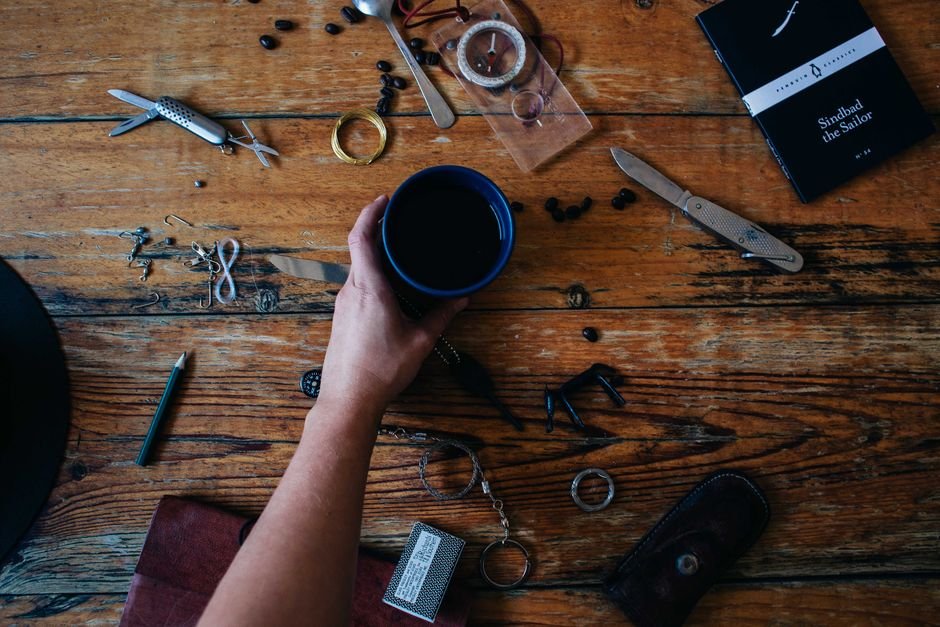 A hand holding a coffee cup amidst various items on a rustic wooden table, ideal for lifestyle themes.