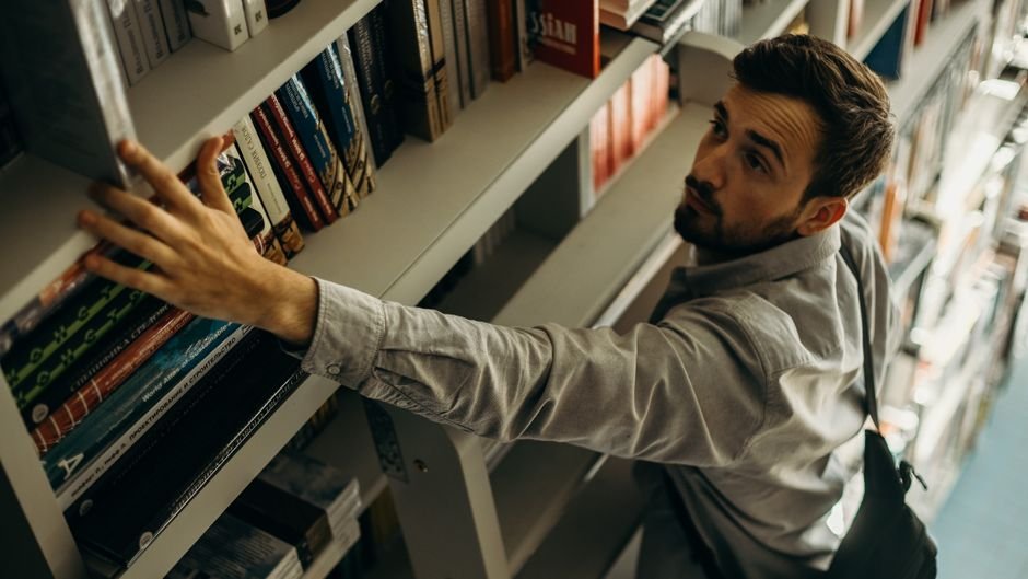A man reaching for a book on a library bookshelf with focus and determination.