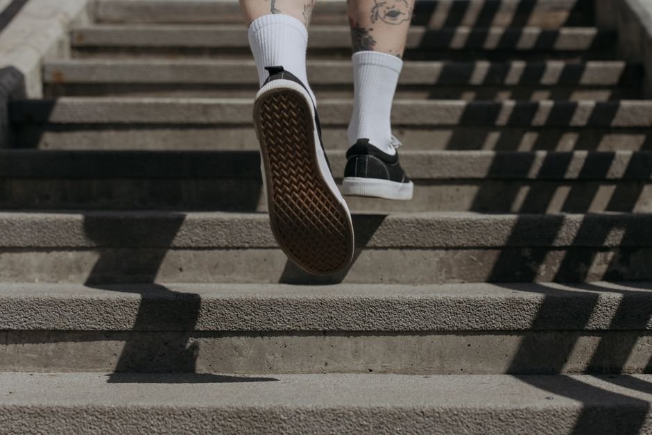 Athletic person wearing black sneakers and white socks jogging up concrete stairs outdoors.