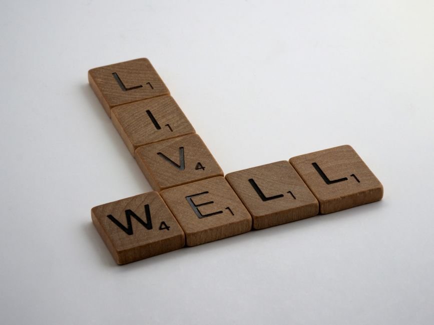Wooden Scrabble tiles spelling 'Live Well' on a white surface. Perfect for motivational content.