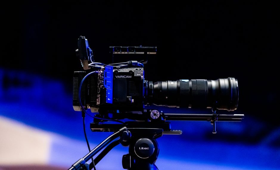 Side view of a professional video camera with lens on a tripod, ready for filming.