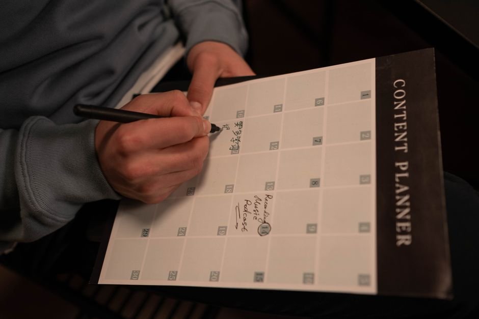 Close-up of hands writing in a content planner for organizational purposes.