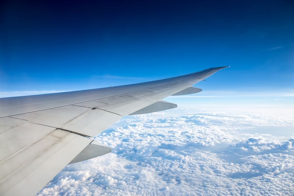Stunning view from an airplane wing flying above the clouds with clear blue sky.