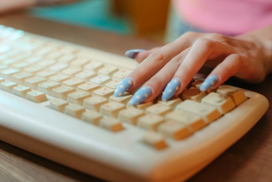 Closeup of a hand with polka dot nails typing on a vintage keyboard, emphasizing retro technology.